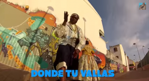 Das Bild zeigt den Rapper Lory Money in traditioneller Kleidung vor eine Graffittiwand in Valencia